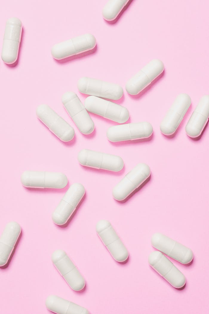 about-01 White medicinal capsules scattered on a vibrant pink background, symbolizing healthcare and wellness.
