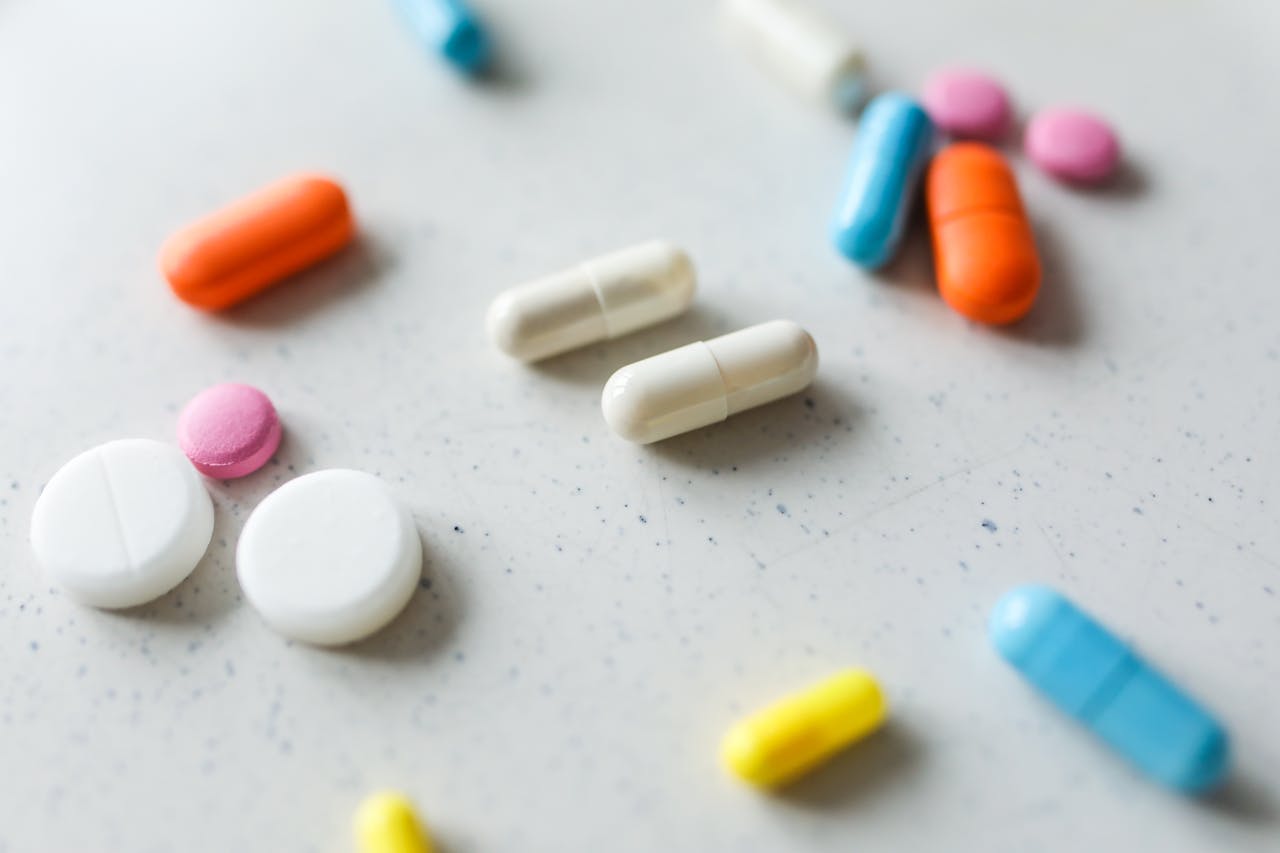 hero-img-02 Close-up view of assorted colorful pills and tablets scattered on a white surface.
