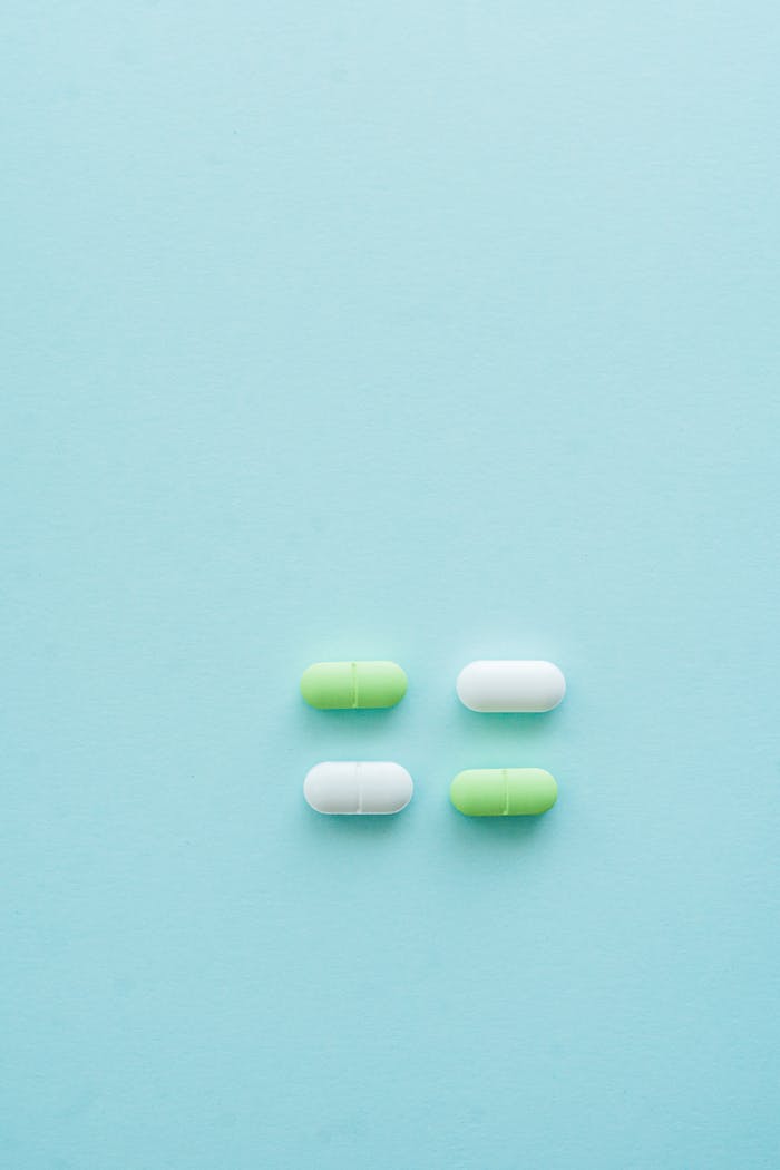 our-services-2 Four green and white capsules arranged on a pastel blue background create a minimalist aesthetic.